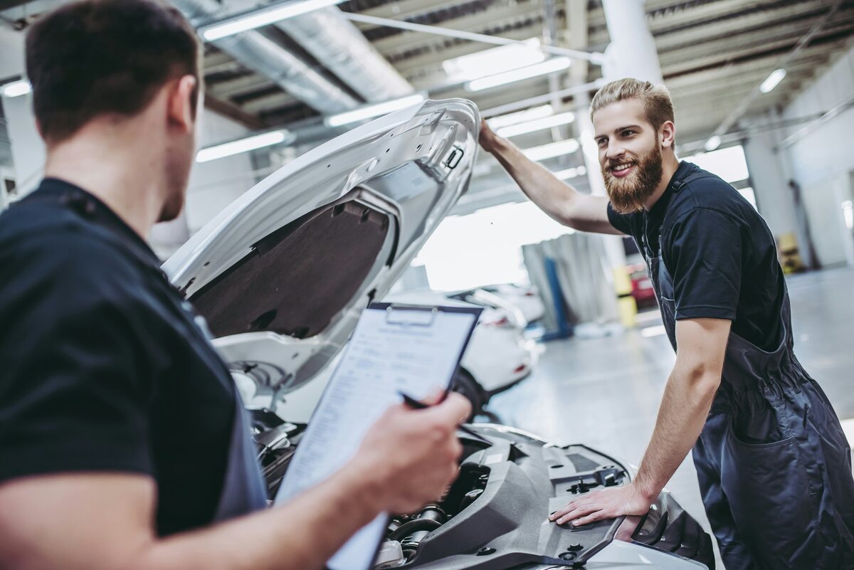 A bearded tradesman working under the hood of a car in a shop