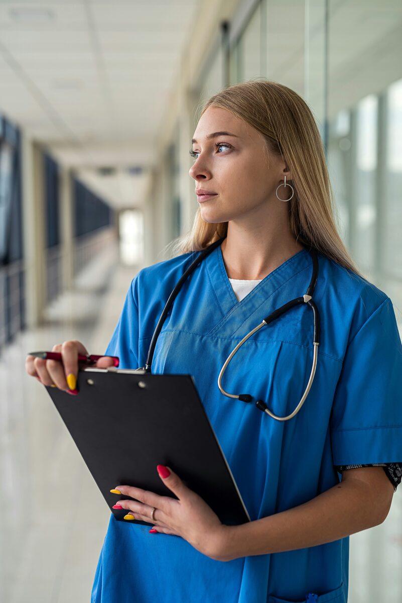 A nurse in scrubs looking ahead in a hospital corridor