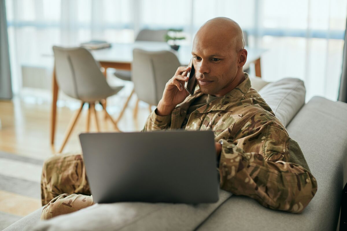 A service member in camo on a couch using a laptop